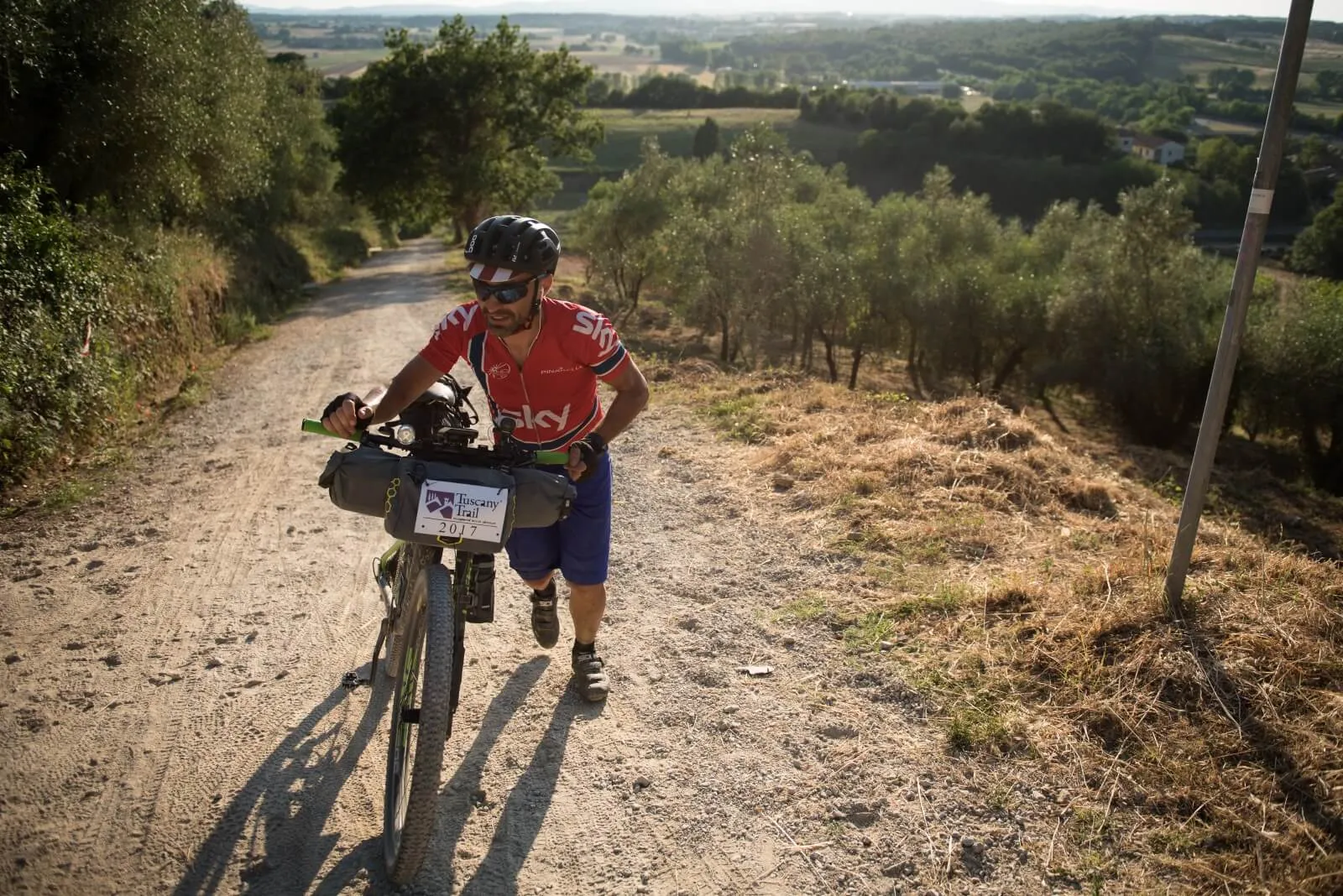 A rider pushing the bike uphill on a white road
