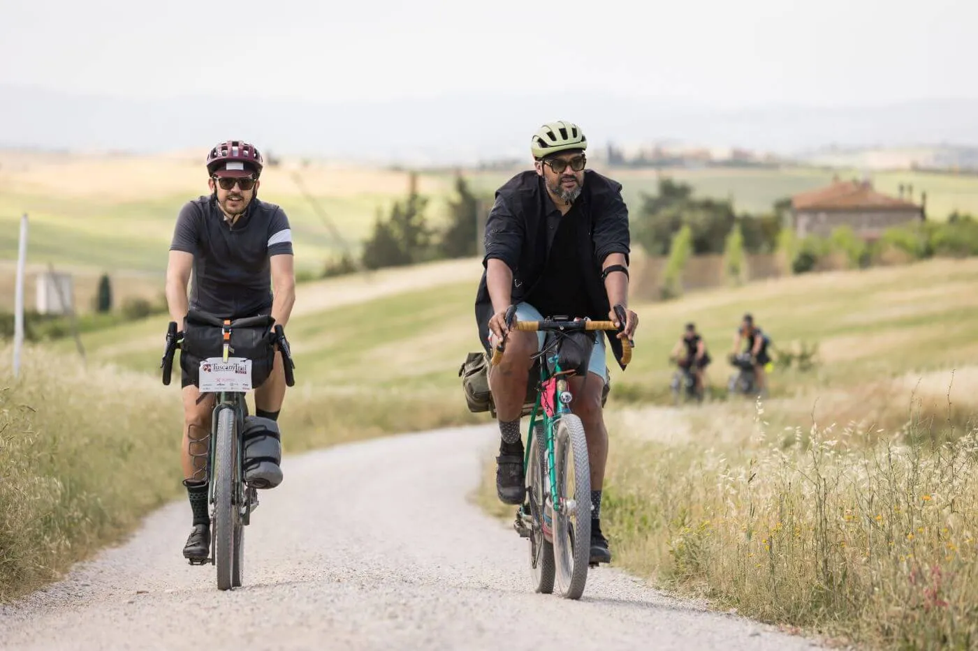 Two riders on a white road through wheat fields
