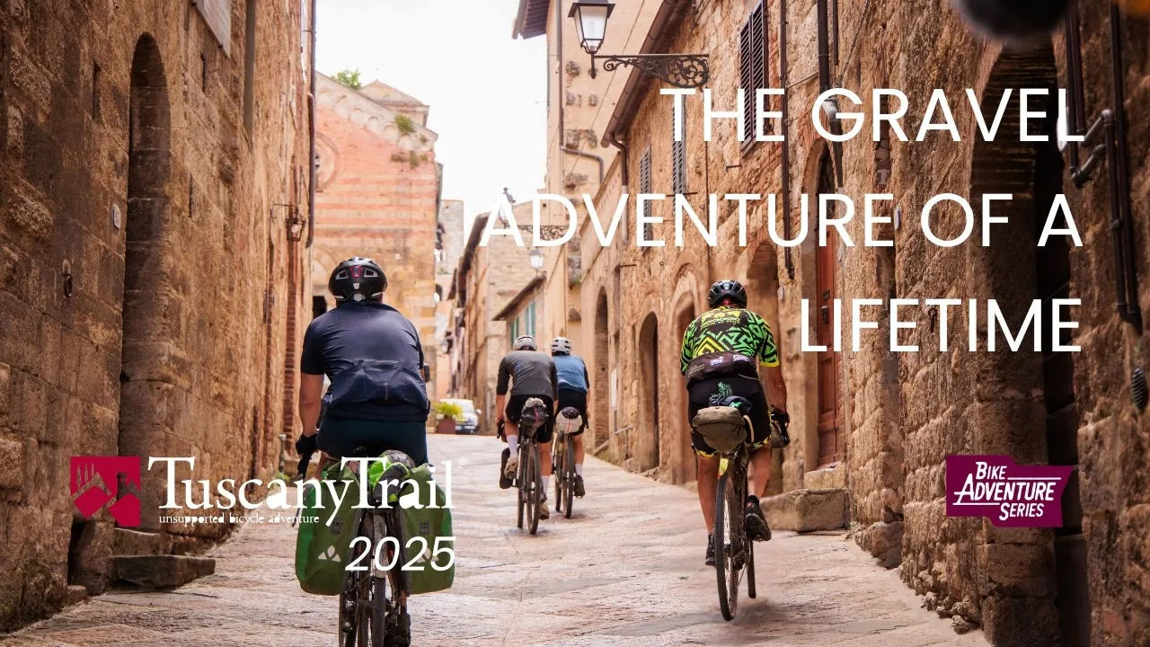 Four riders with bikepacking bags ride up the stone alley of a Tuscan village