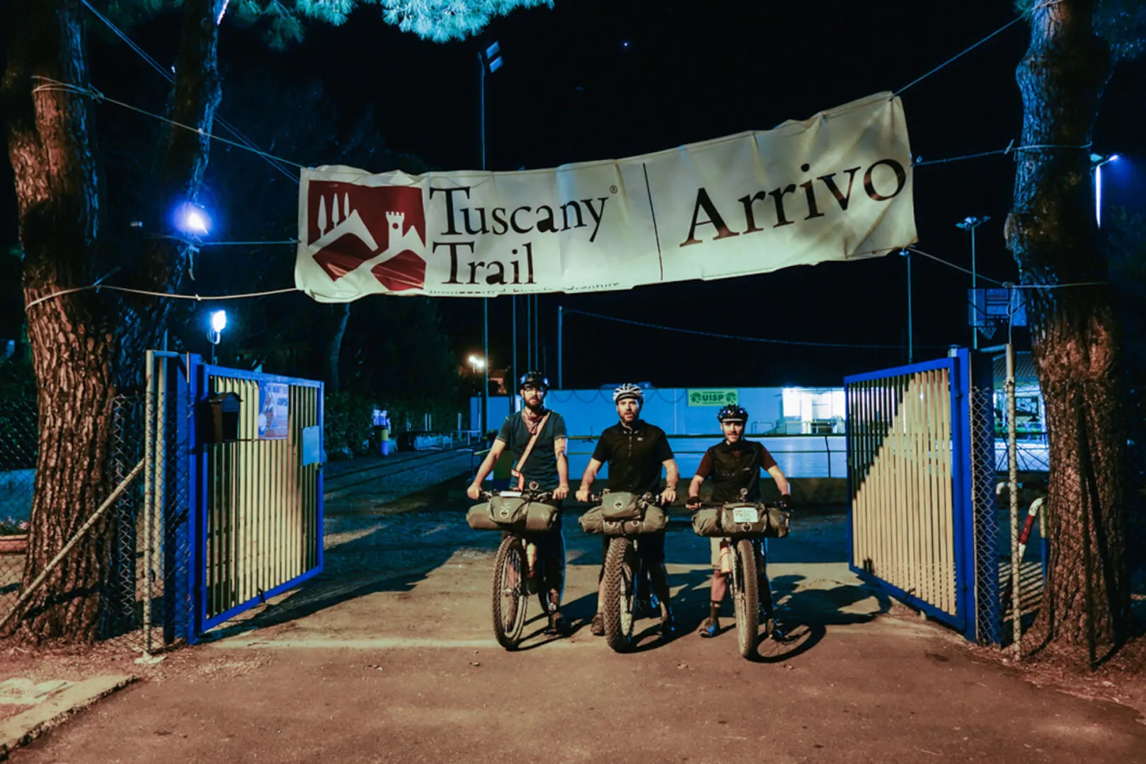 Three riders under the finish arch at night