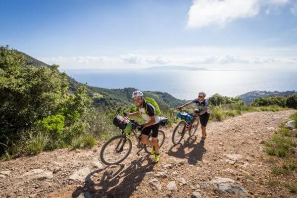 Two riders on a gravel road with the sea on the horizon
